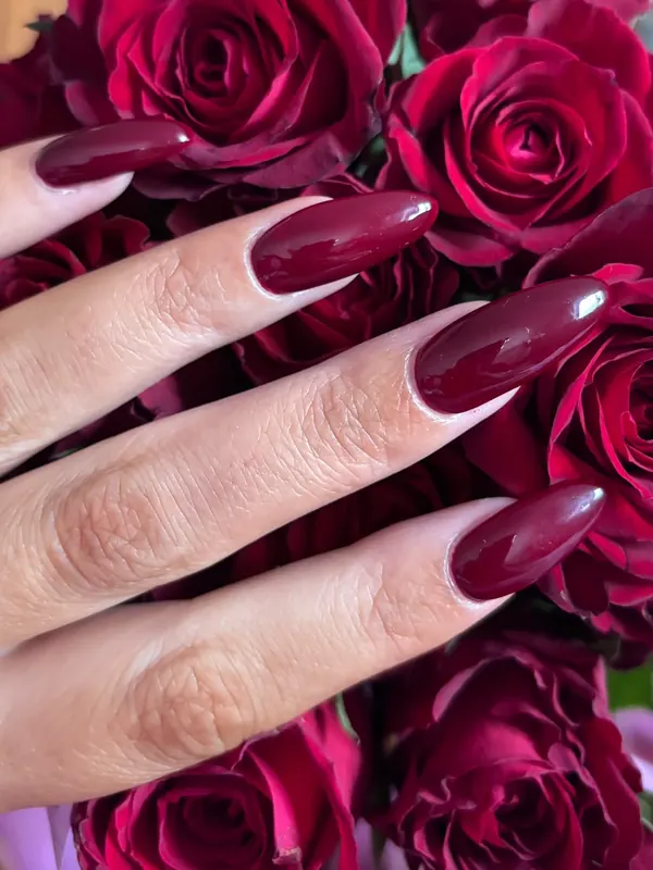 Long almond nails in glossy deep cherry red, photographed against red roses
