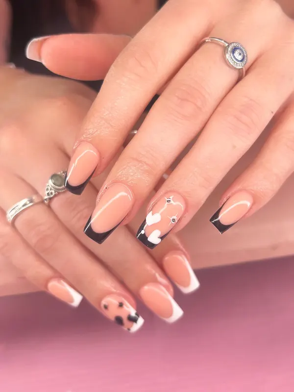 Square nude nails with black and white French tips and cow print heart accent nails