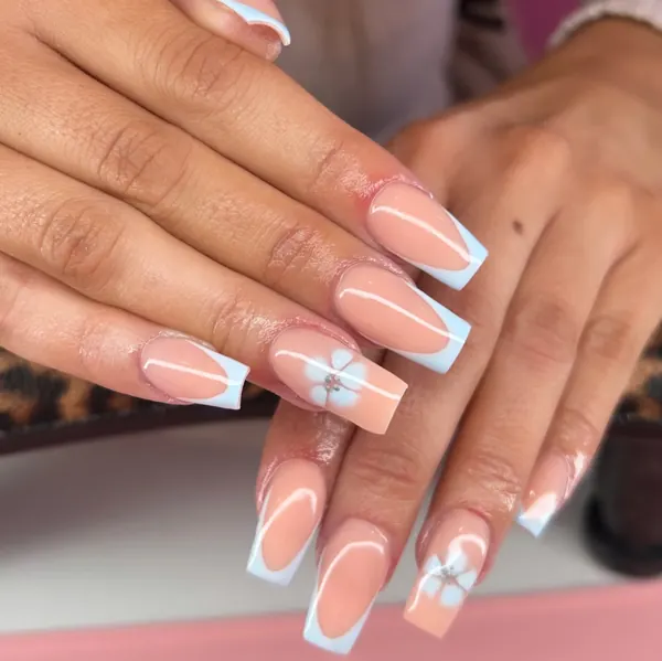 Long square nude nails with baby blue French tips and a white flower accent with a gem