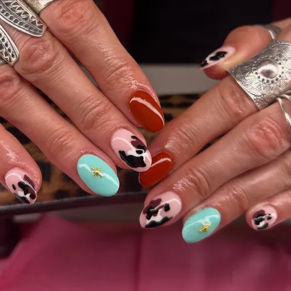 Short rounded nails mixing burnt orange, pink cow print and turquoise with gold star studs