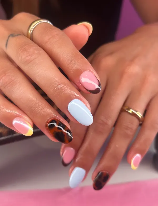 Short almond nails mixing tortoiseshell print, solid baby blue and pink French tips with a yellow swirl